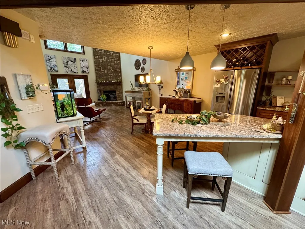 Kitchen featuring a textured ceiling, a fireplace, stainless steel fridge, light wood-type flooring, and hanging light fixtures