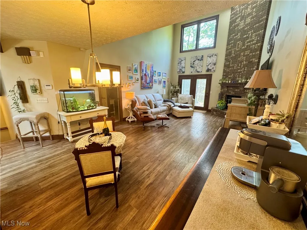 Living area with a textured ceiling, wood finished floors, a fireplace with raised hearth, and high vaulted ceiling