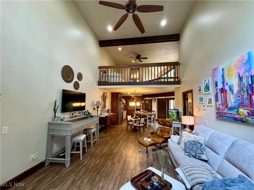 Living area featuring high vaulted ceiling, ceiling fan, dark wood finished floors, beam ceiling, and a chandelier