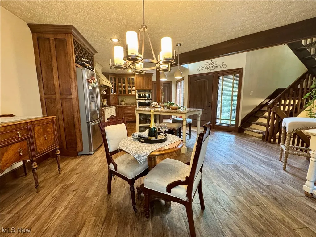 Dining space with stairway, a chandelier, wood finished floors, and a textured ceiling