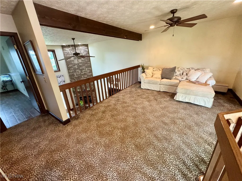 Carpeted living area with a ceiling fan, a textured ceiling, beam ceiling, and recessed lighting