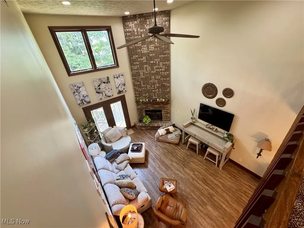 Living room featuring recessed lighting, ceiling fan, a fireplace, wood finished floors, and a high ceiling