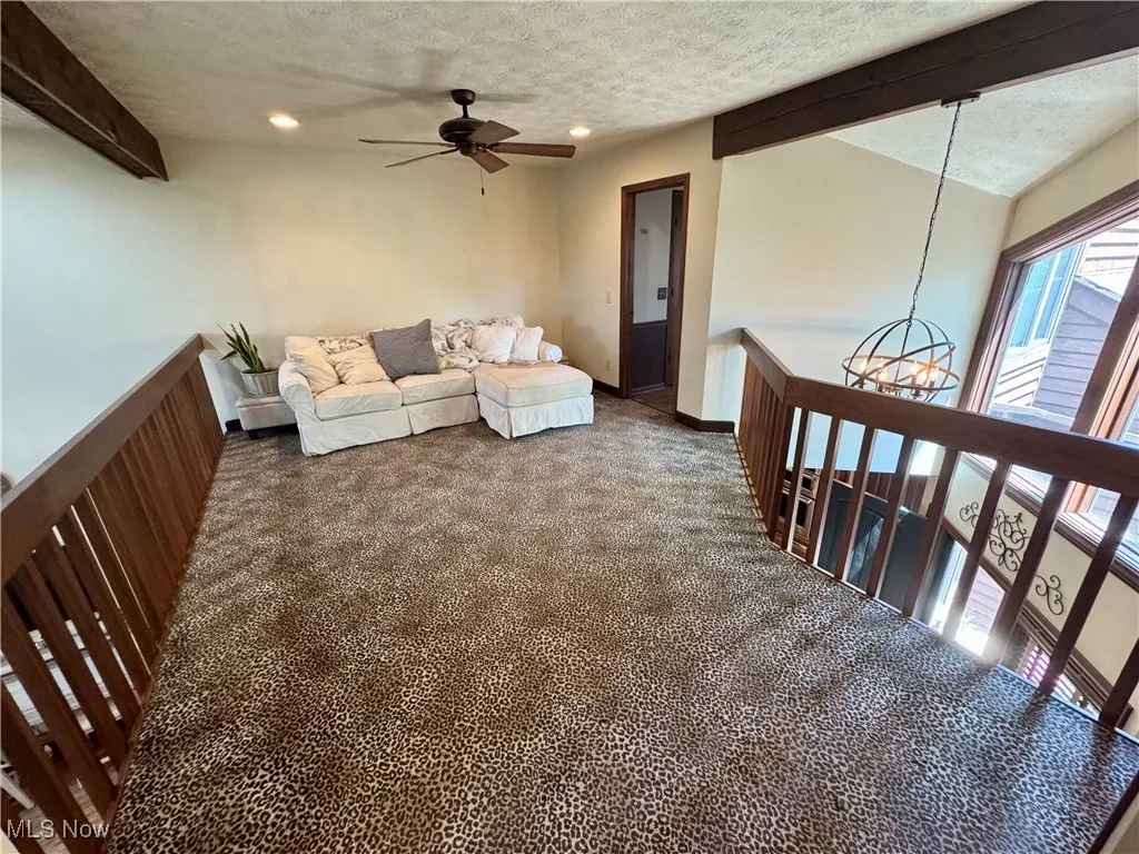 Carpeted living room with a ceiling fan, a textured ceiling, beam ceiling, recessed lighting, and a chandelier