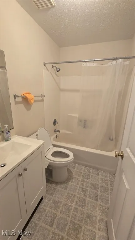 Full bath with vanity, shower / tub combo with curtain, and a textured ceiling