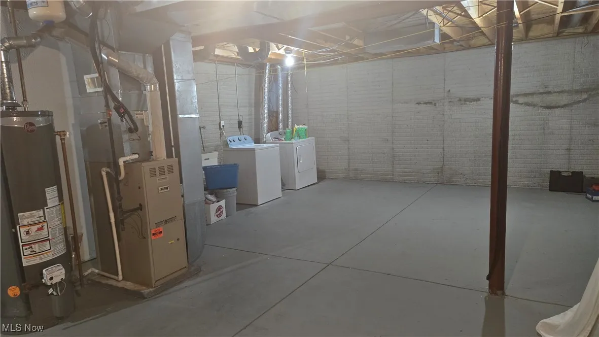 Unfinished basement featuring washer and clothes dryer, gas water heater, and heating unit
