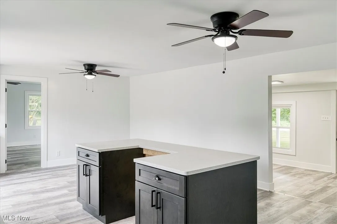 Kitchen with ceiling fan, light wood-style floors, light countertops, and a kitchen island