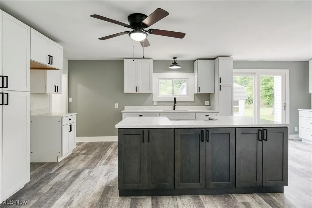 Kitchen with ceiling fan, light wood-style flooring, white cabinets, a kitchen island, and light countertops