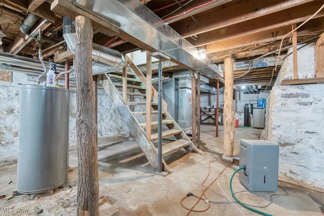 Unfinished basement with water heater, stairway, and heating unit