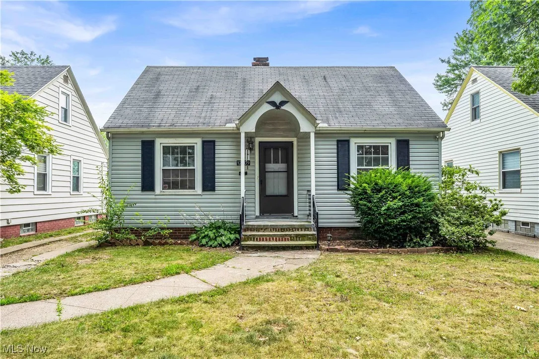 View of front of house with a front yard, a shingled roof, and a chimney