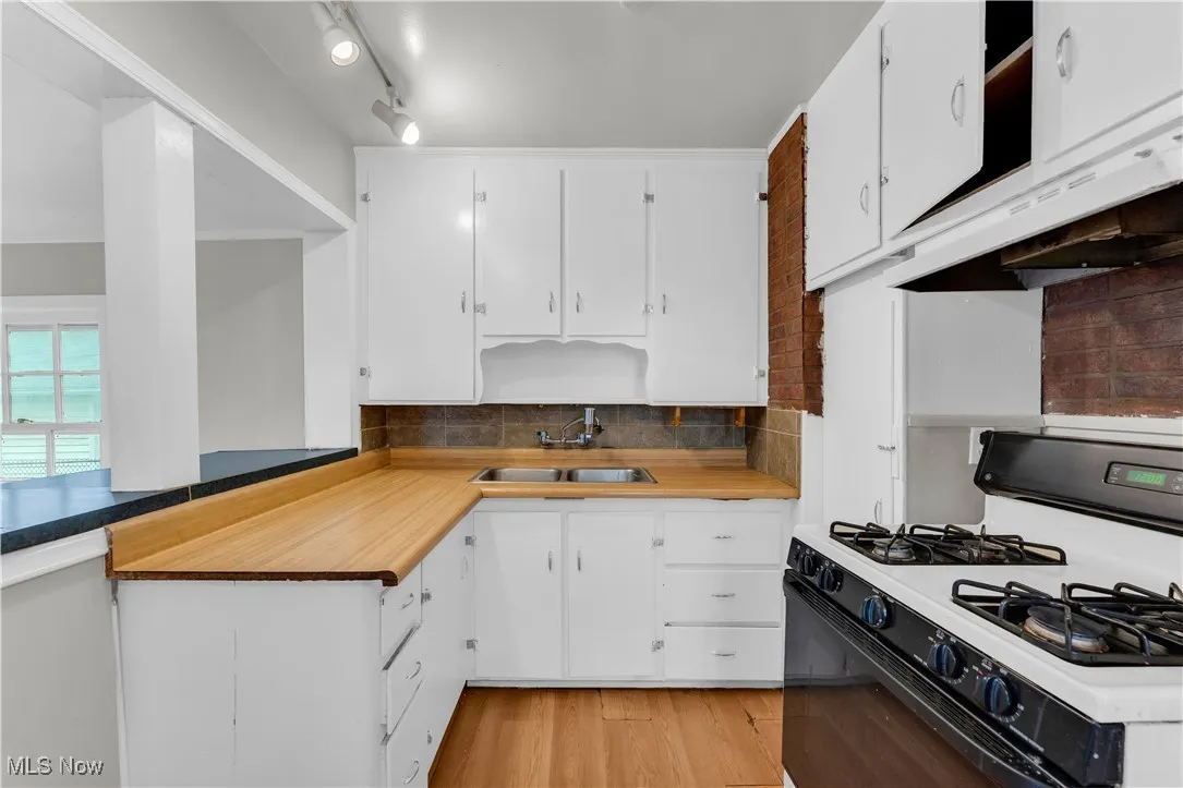Kitchen with gas range oven, white cabinetry, tasteful backsplash, under cabinet range hood, and light wood-style floors