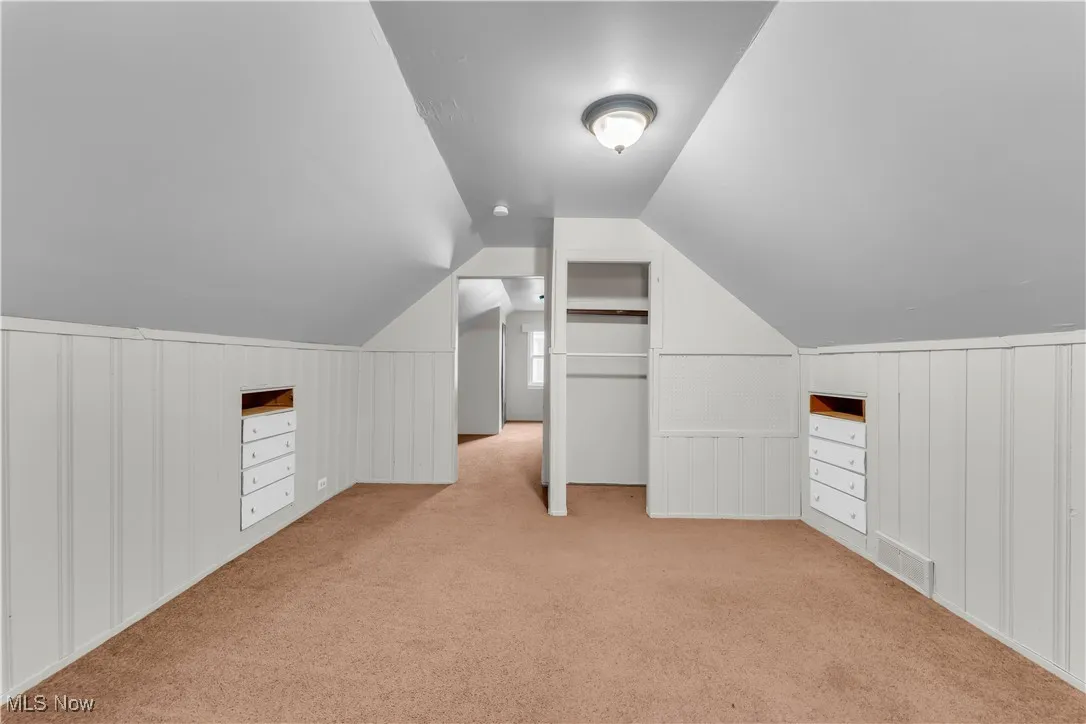 Additional living space featuring carpet flooring, a decorative wall, and vaulted ceiling