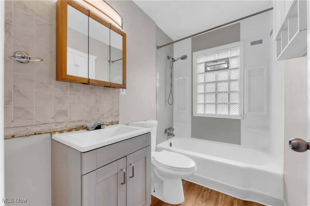 Full bathroom with vanity, decorative backsplash, washtub / shower combination, and wood finished floors