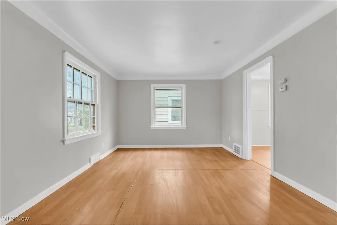 Spare room featuring healthy amount of natural light, light wood-style floors, and ornamental molding