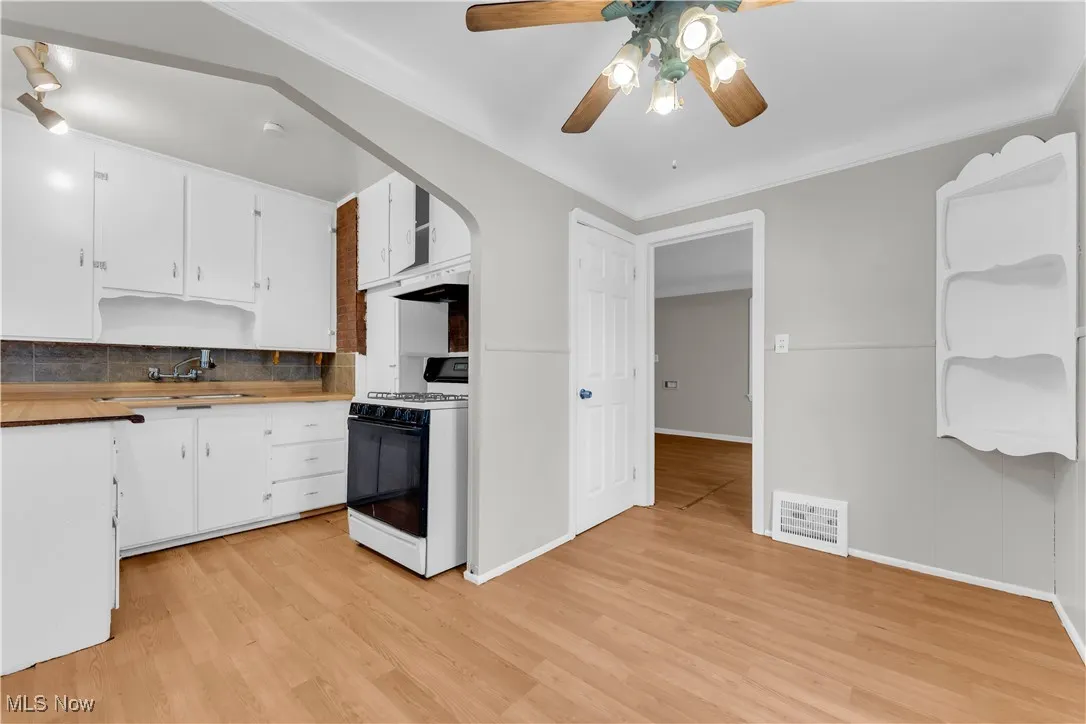 Kitchen featuring gas range, decorative backsplash, light wood-style floors, and ceiling fan