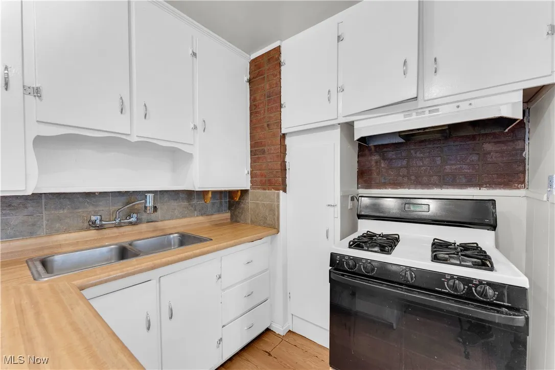 Kitchen with gas range oven, light countertops, under cabinet range hood, and white cabinetry