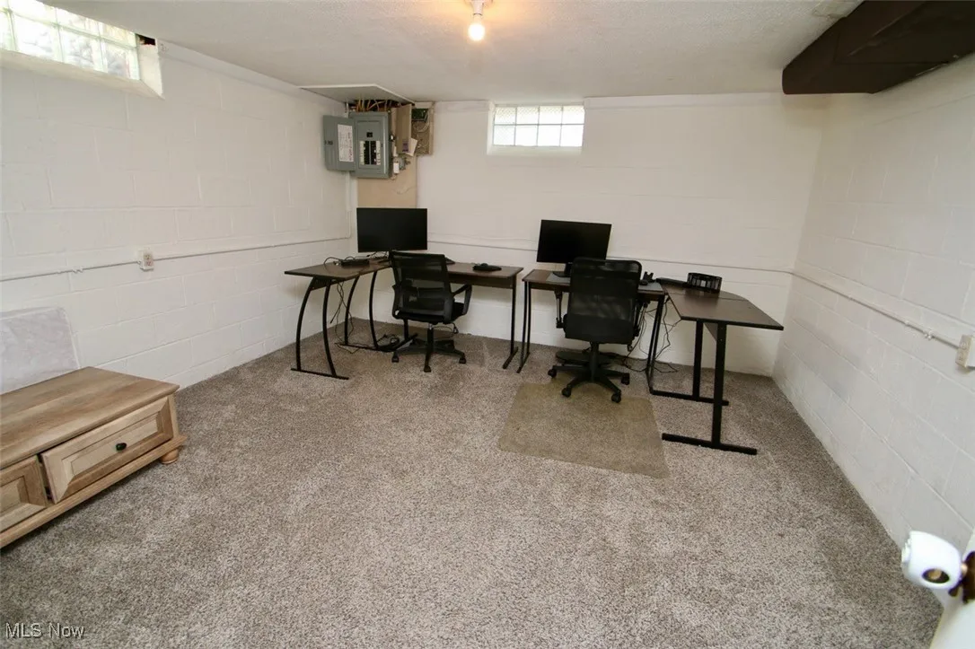 Carpeted office featuring electric panel and concrete block wall