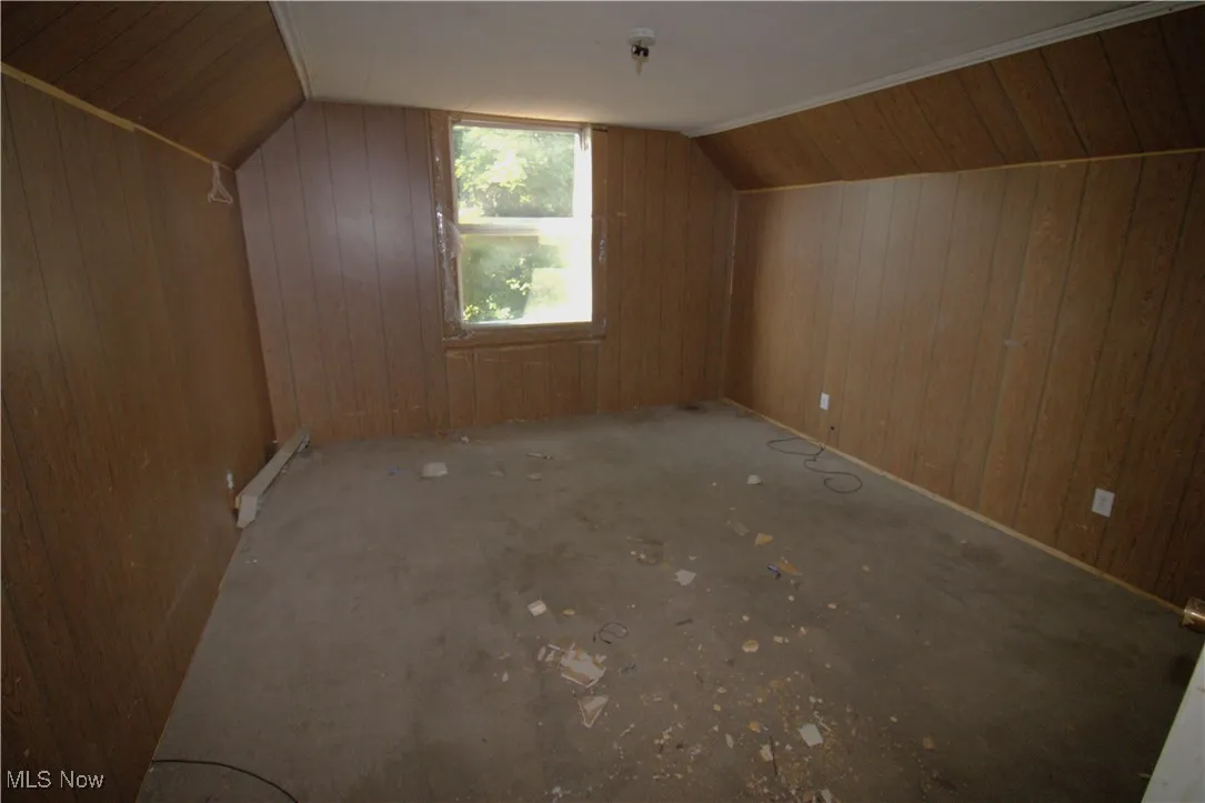 Additional living space featuring lofted ceiling, a baseboard radiator, and wooden walls