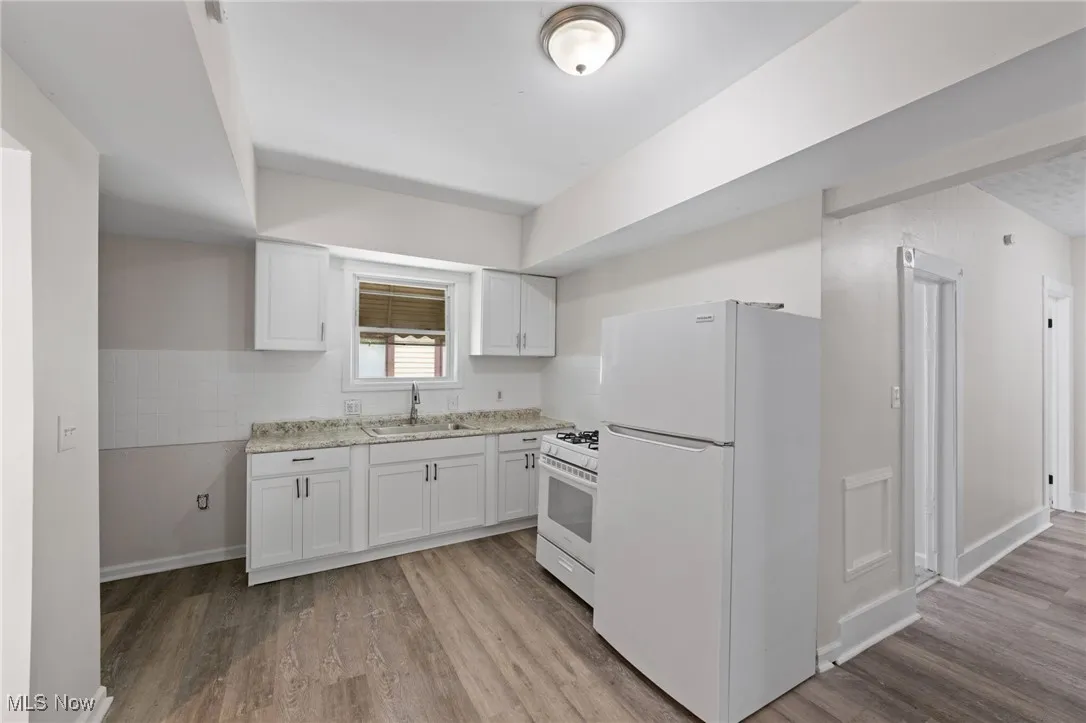 Kitchen with white appliances, white cabinetry, light wood-type flooring, and light stone countertops