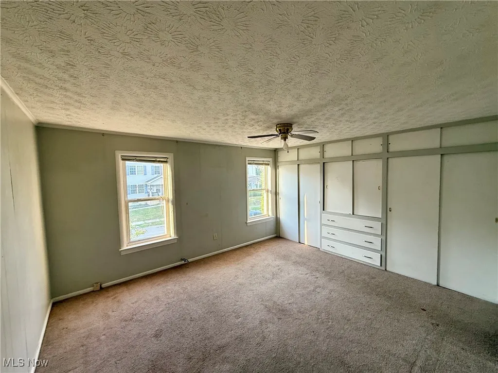 Unfurnished bedroom featuring a textured ceiling, carpet flooring, and a ceiling fan