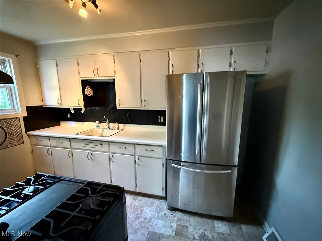 Kitchen featuring freestanding refrigerator, range with gas cooktop, light countertops, white cabinets, and backsplash