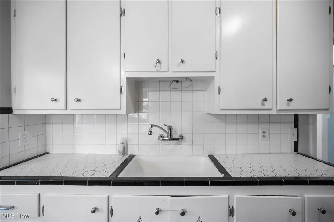 Kitchen with white cabinetry, decorative backsplash, and tile countertops