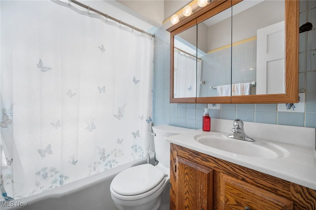 Bathroom featuring tile walls, vanity, shower / bath combo and decorative backsplash