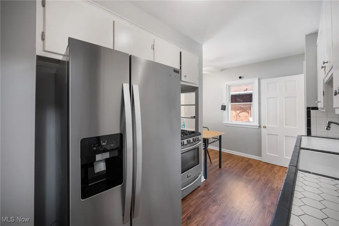 Kitchen featuring stainless steel appliances, white cabinetry, dark wood-style floors, tasteful backsplash, and tile counters