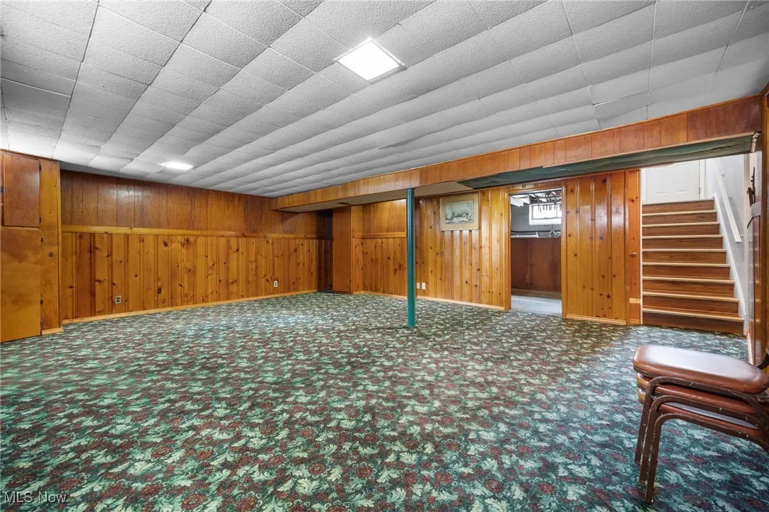 Below grade area with wooden walls, carpet floors, and stairway