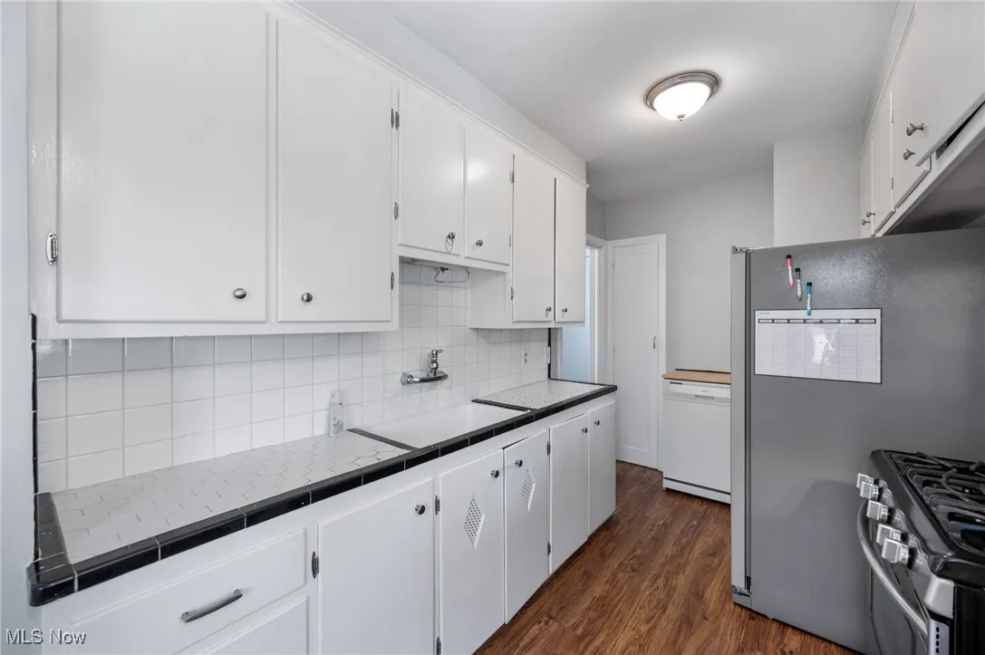 Kitchen featuring appliances with stainless steel finishes, white cabinets, tasteful backsplash, dark wood-style floors, and tile countertops