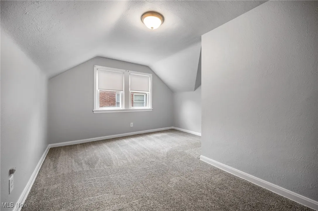 Bedroom featuring carpet, vaulted ceiling, and a textured ceiling