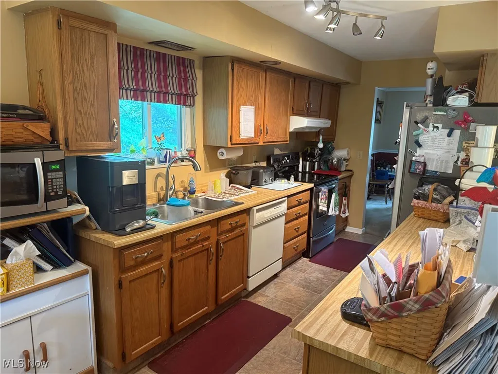 Kitchen with appliances with stainless steel finishes, under cabinet range hood, and brown cabinetry
