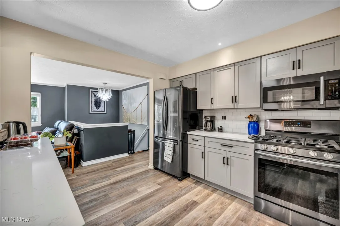 Kitchen featuring stainless steel appliances, light wood-style floors, backsplash, a chandelier, and gray cabinets