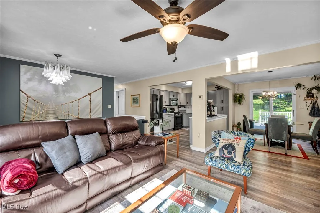 Living room with a chandelier, light wood-type flooring, crown molding, and ceiling fan