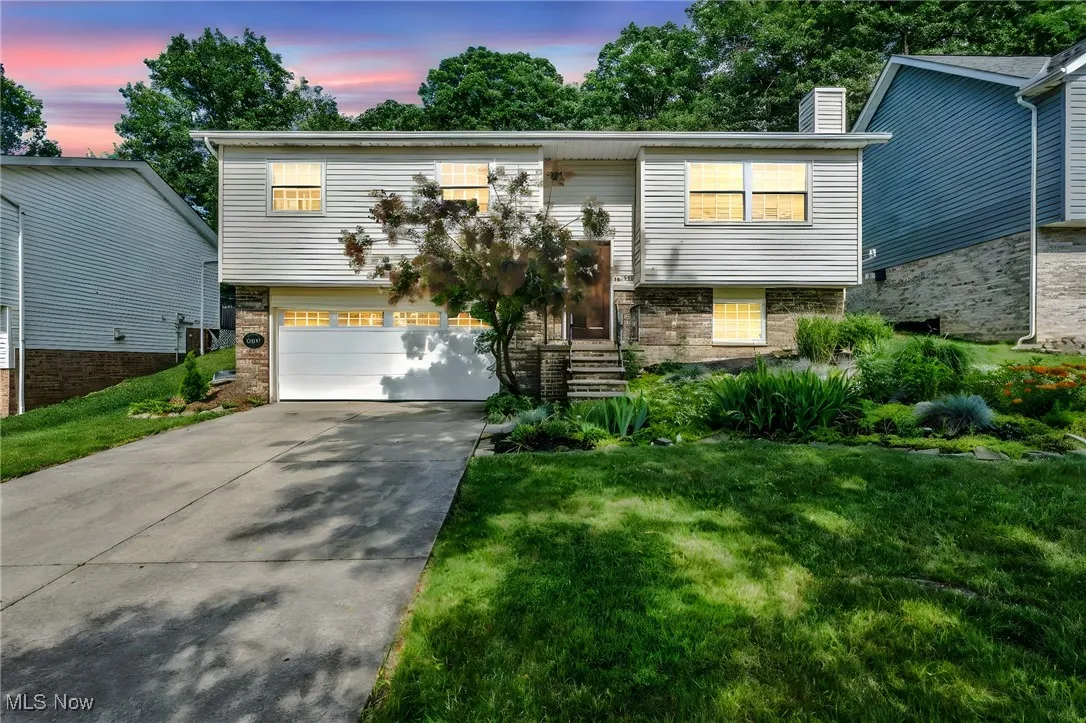 Raised ranch with driveway, brick siding, a chimney, and a yard