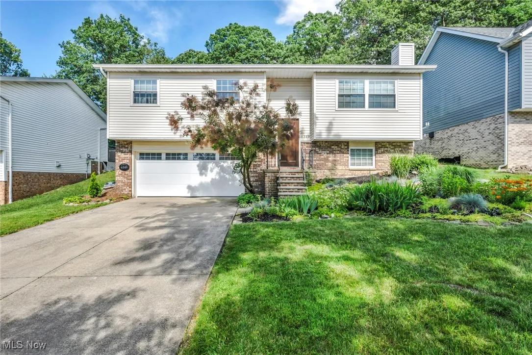 Raised ranch with a garage, brick siding, concrete driveway, a chimney, and a front yard