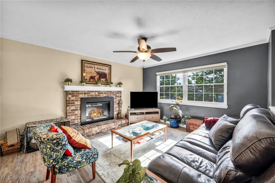 Living room featuring a ceiling fan, wood finished floors, a brick fireplace, and crown molding