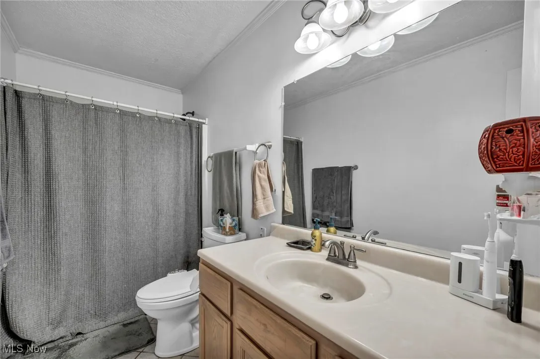 Full bath with vanity, a textured ceiling, tile patterned floors, and ornamental molding