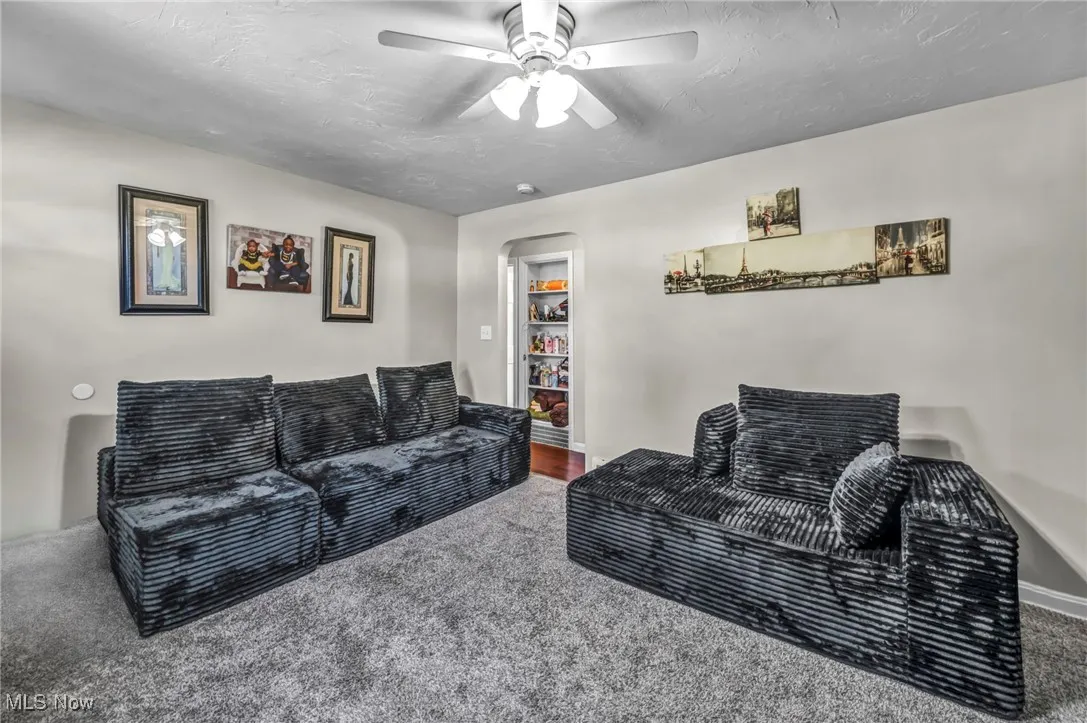 Carpeted living area with arched walkways, ceiling fan, and a textured ceiling