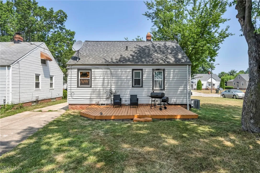 Rear view of property with a chimney, a shingled roof, a wooden deck, and a lawn