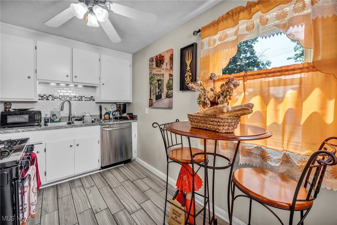 Kitchen with decorative backsplash, black appliances, white cabinets, ceiling fan, and light wood-style floors