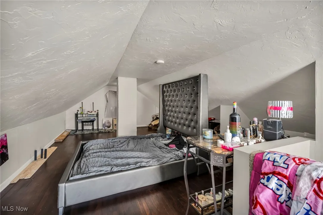 Bedroom featuring vaulted ceiling, wood finished floors, and a textured ceiling