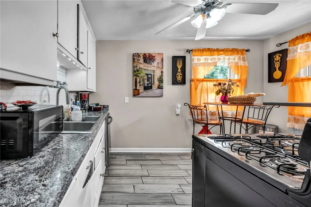 Kitchen with black appliances, a ceiling fan, white cabinetry, tasteful backsplash, and dark countertops
