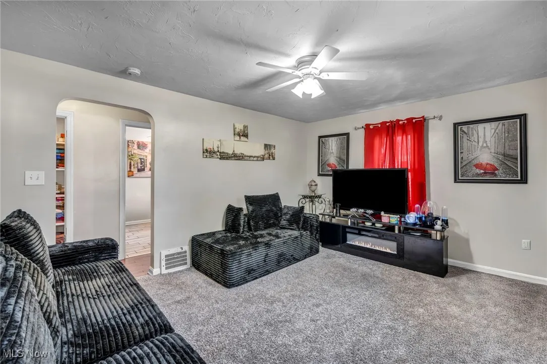 Living room featuring arched walkways, a ceiling fan, and carpet floors