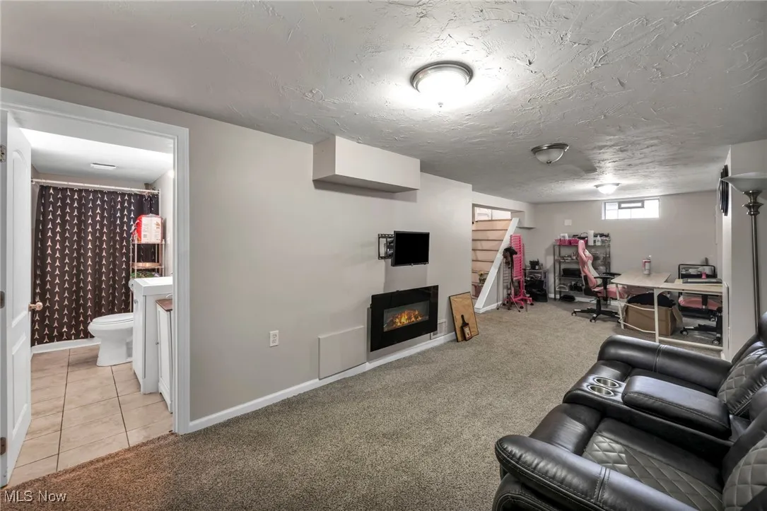 Living room featuring light carpet, light tile patterned floors, and a warm lit fireplace