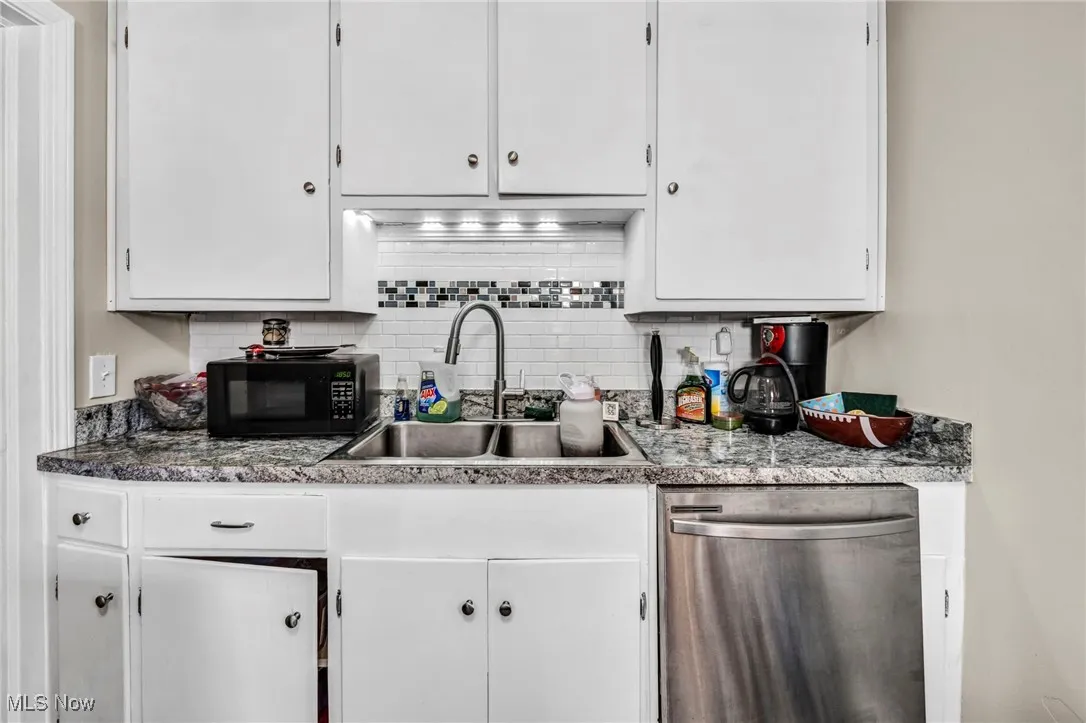 Kitchen with stainless steel dishwasher, white cabinets, decorative backsplash, and black microwave