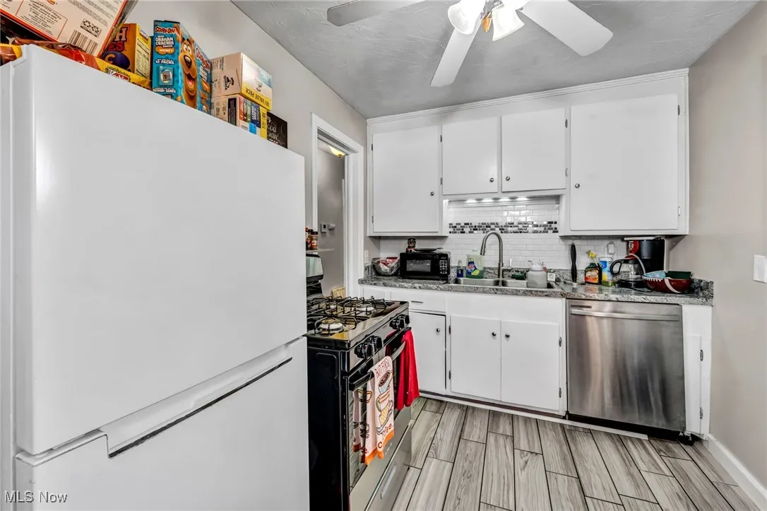 Kitchen featuring freestanding refrigerator, gas stove, stainless steel dishwasher, backsplash, and white cabinetry