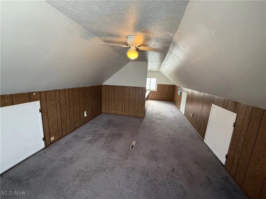 Additional living space featuring wooden walls, a ceiling fan, vaulted ceiling, a textured ceiling, and carpet flooring