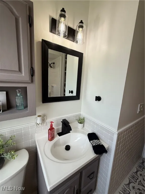 Bathroom featuring vanity, wainscoting, and tile walls