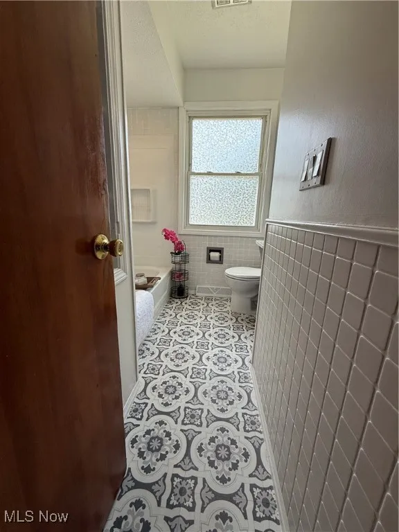 Full bathroom with a tub to relax in, tile walls, and a wainscoted wall