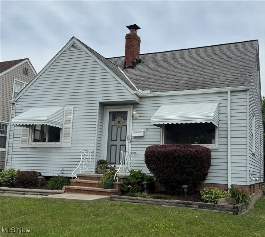 View of front facade featuring a shingled roof, a chimney, and a front lawn